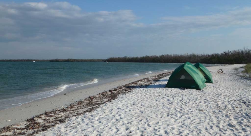 two green tents are set up on the white sand of a beach